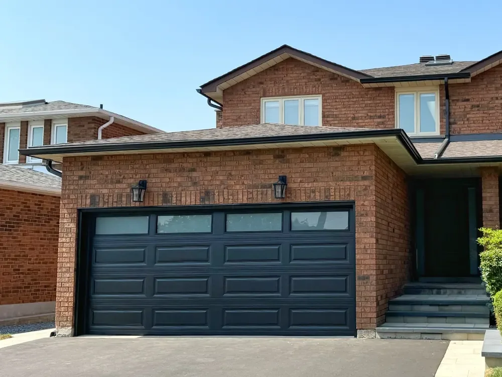 Black long raised-panel garage door with windows on a home in Oakville