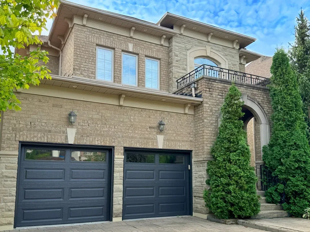 Dark brown long raised-panel garage doors with windows on a home in Oakville