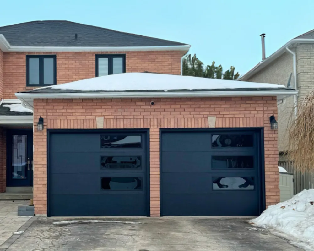 New insulated black garage doors on a brick home with snow on the roof